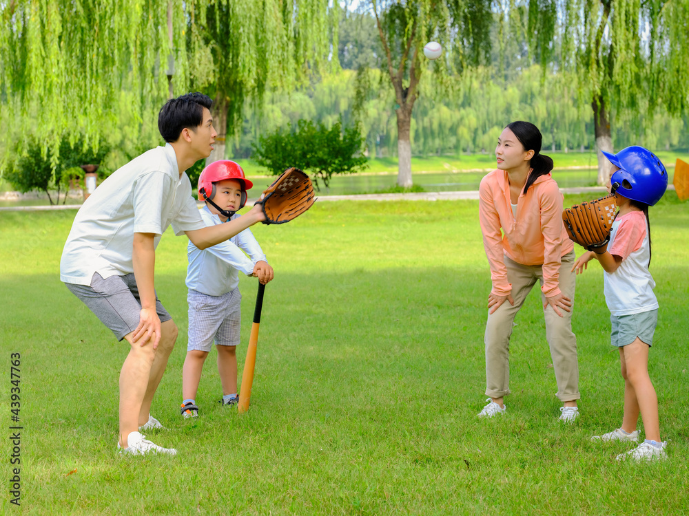 Happy family of four playing baseball in the park