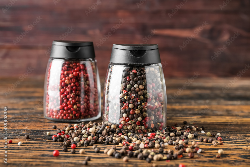 Jars with peppercorns on wooden background