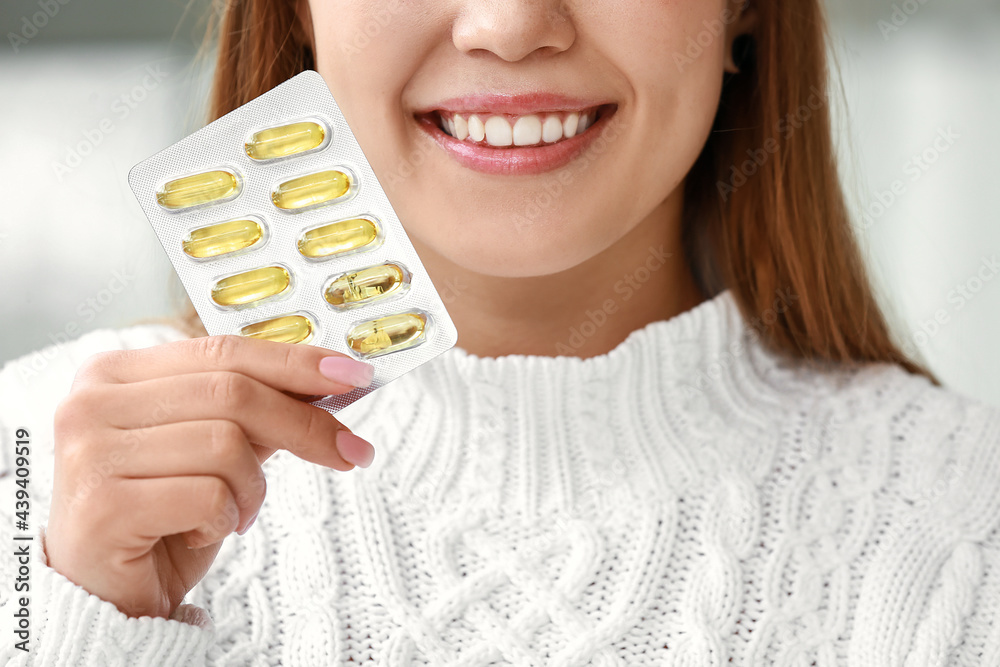 Young woman with fish oil pill at home, closeup