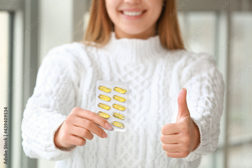 一名年轻女子服用鱼油药丸，在家中竖起大拇指，特写镜头