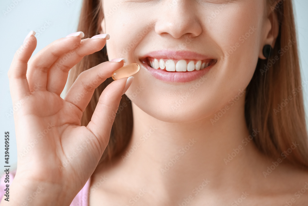 Young woman with fish oil pill on light background, closeup