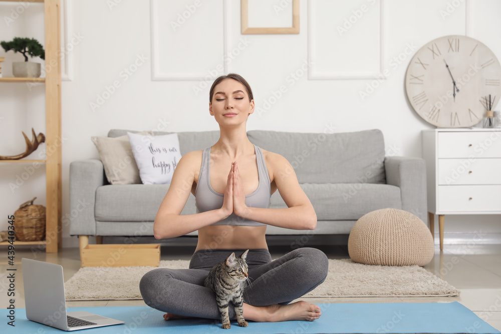 Beautiful young woman with cute cat meditating at home