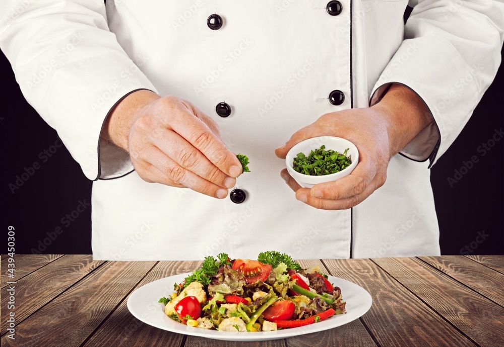 Male chef dressing dish with fresh greens before it is going to be served for restaurant guests