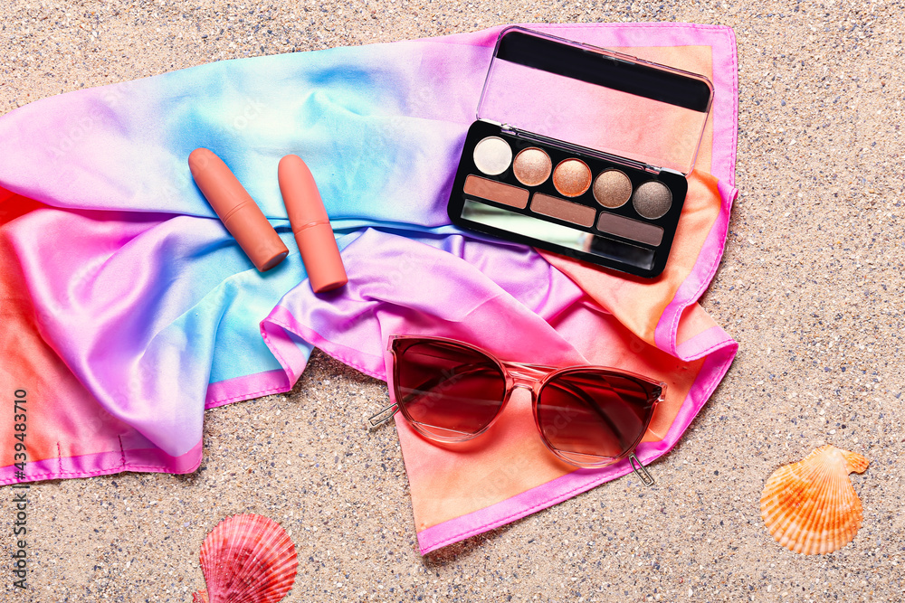 Stylish sunglasses with makeup cosmetics and scarf on sand