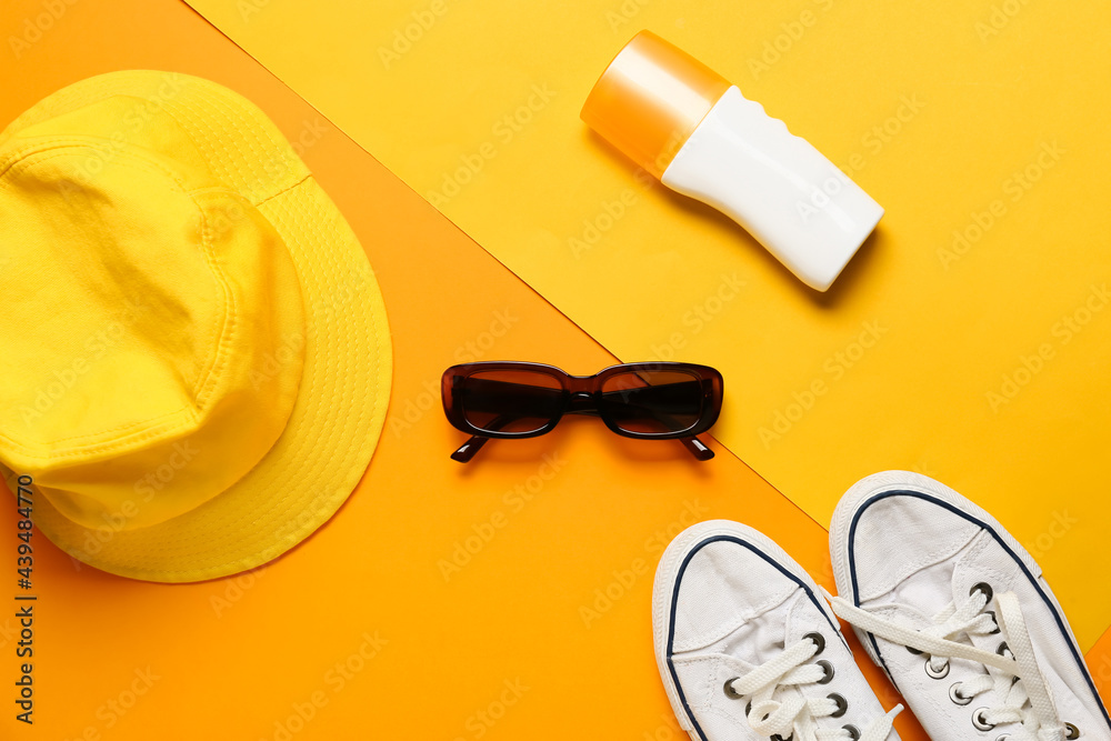 Stylish sunglasses with sunscreen cream, shoes and hat on color background