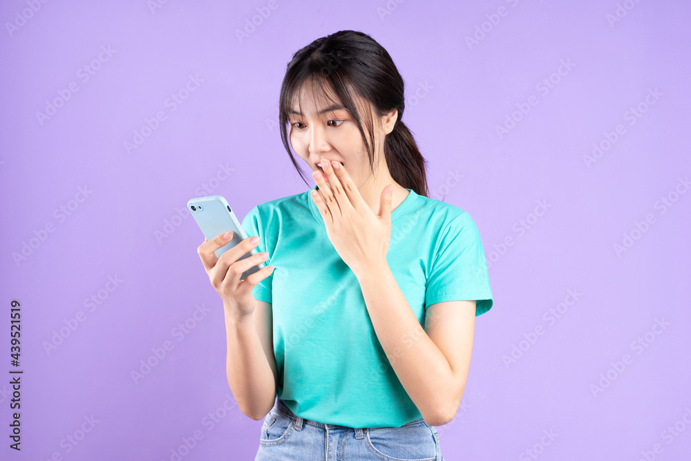 Young asian girl in cyan shirt using phone on purple background