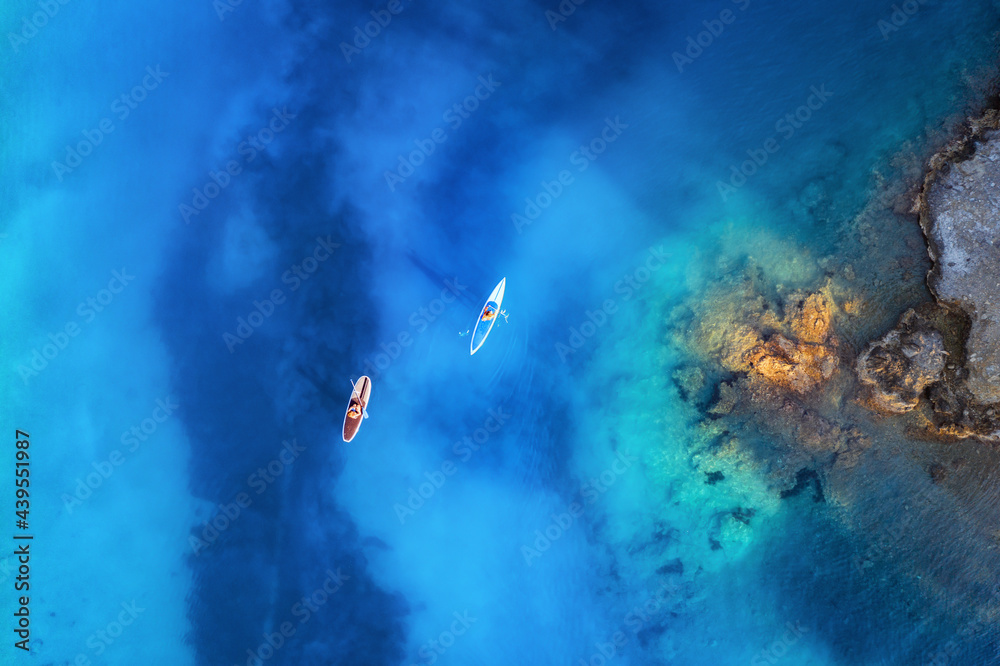 Aerial view of people on floating sup boards on blue sea, rocks, stones at sunset in summer in Olude