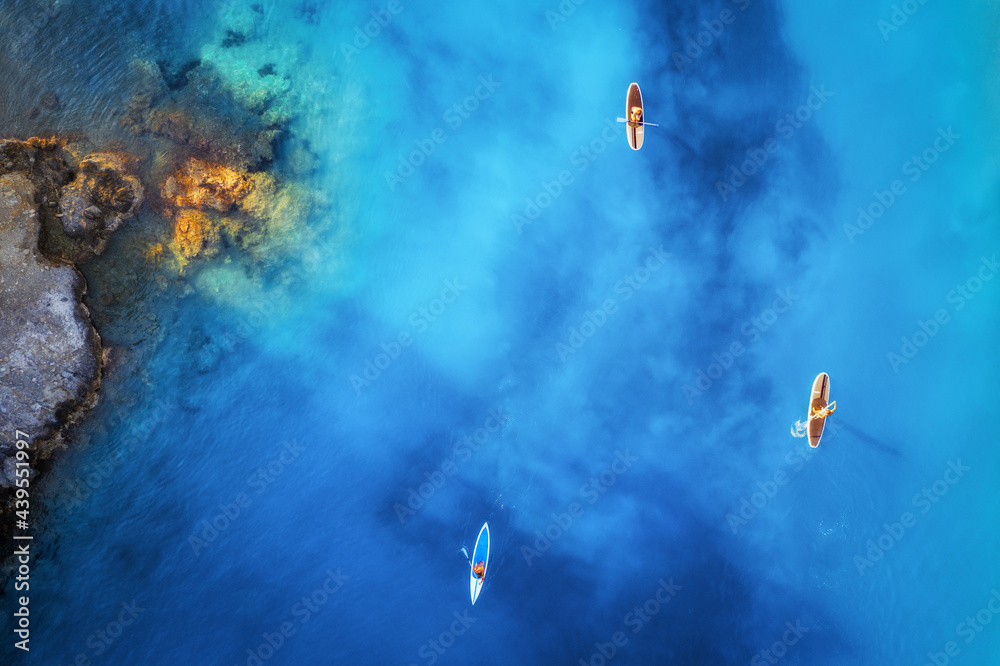 Aerial view of people on floating sup boards on blue sea, rocks, stones at sunset in summer in Olude