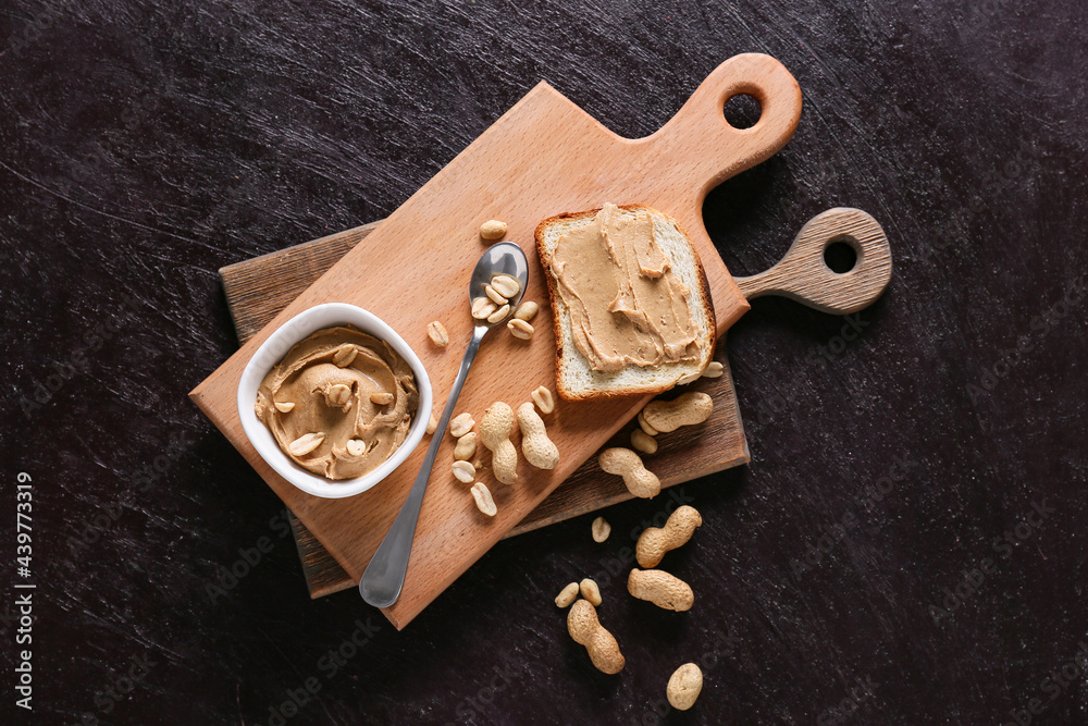 Bowl with tasty peanut butter and bread on dark background