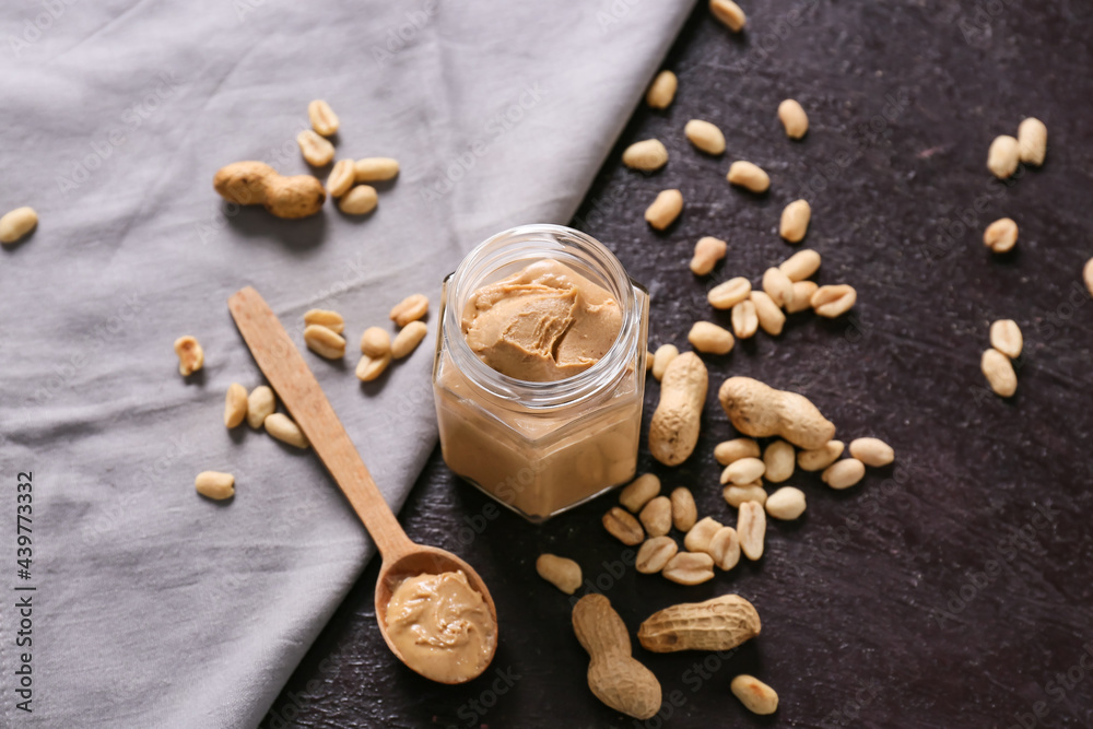 Jar with tasty peanut butter on dark background