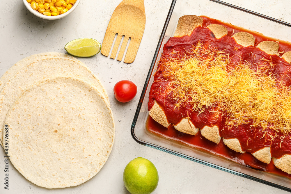 Baking dish with tasty cooked enchilada and ingredients on light background