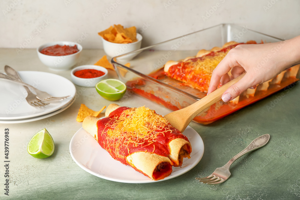 Woman putting hot enchilada from baking dish onto plate