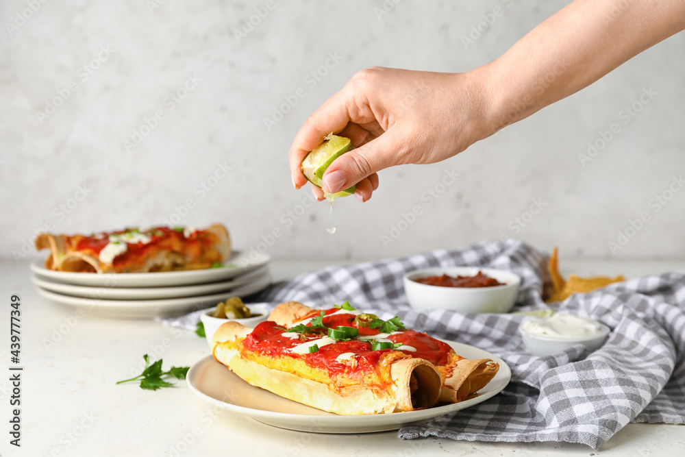 Woman squeezing lime juice onto tasty enchilada on plate