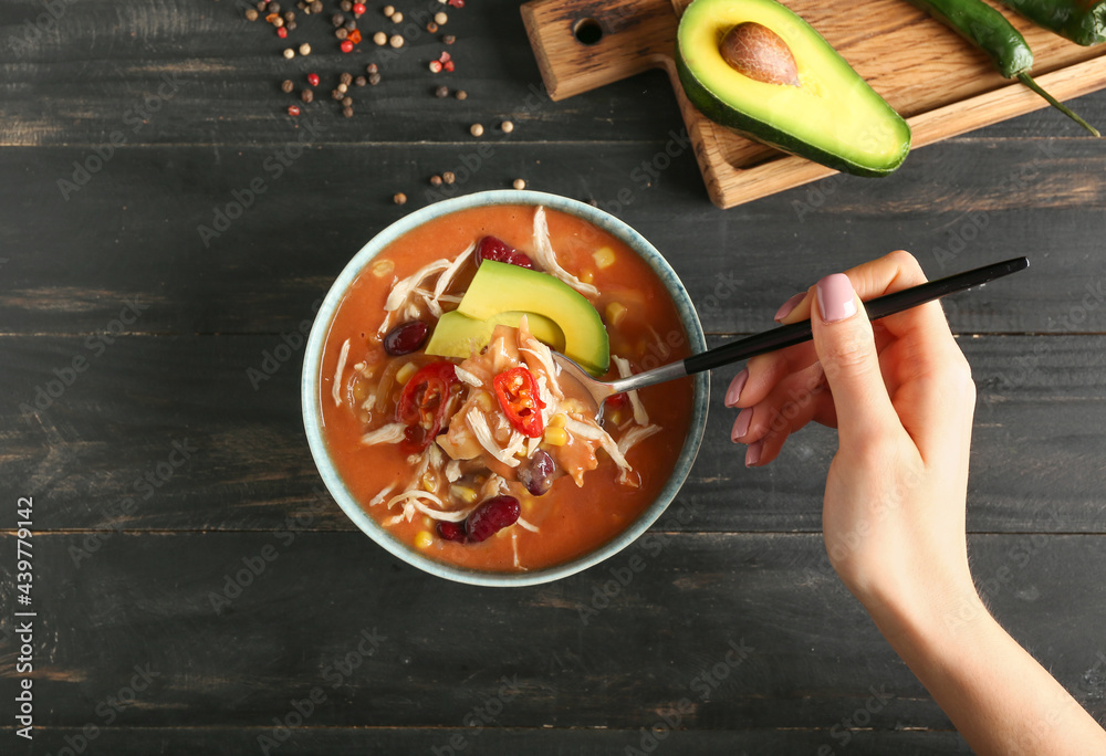 Woman eating tasty chicken enchilada soup from bowl on table