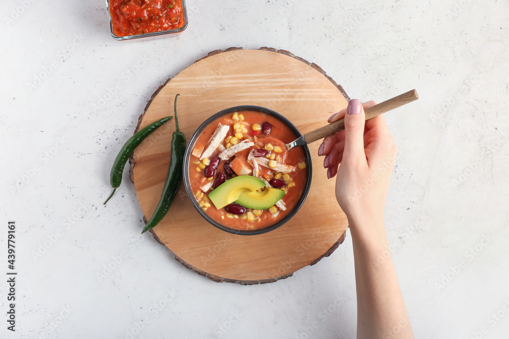 Woman eating tasty chicken enchilada soup from bowl on table