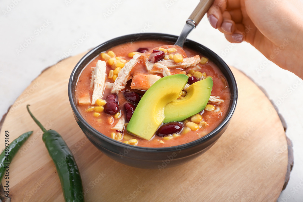 Woman eating tasty chicken enchilada soup from bowl on table