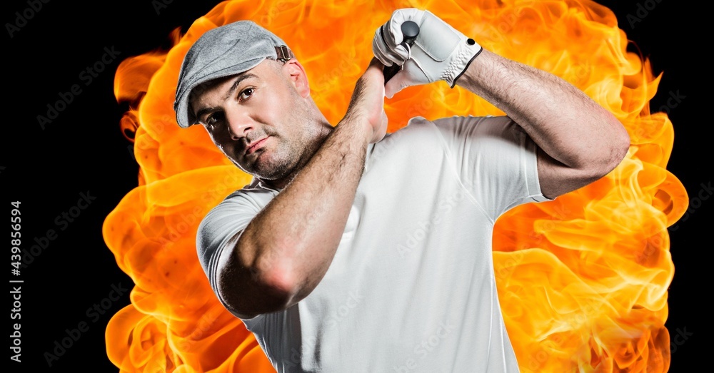 Portrait of caucasian male golf player swinging club against fire flame effect on black background