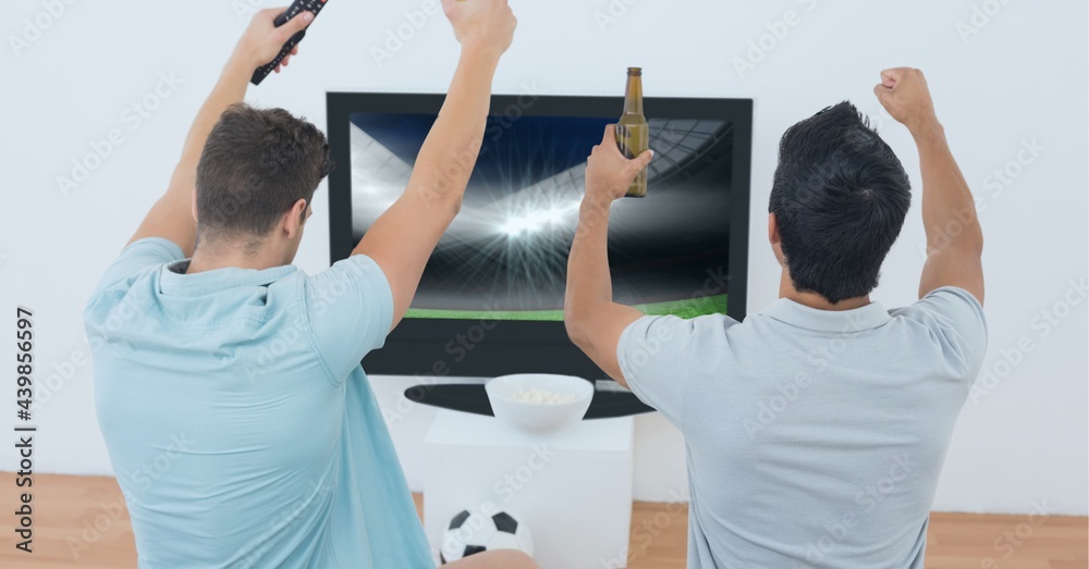 Rear view of two male friends holding beers and cheering while watching sports on tv