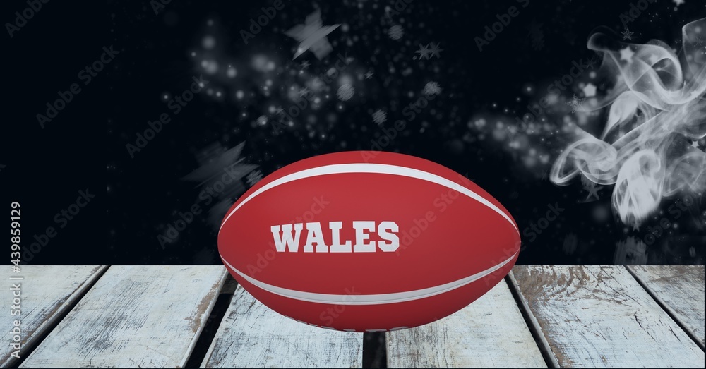 Red rugby ball with wales text over wooden surface against smoke effect on black background