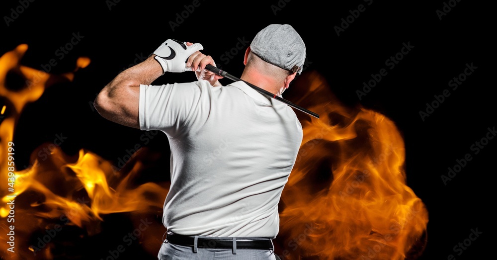 Rear view of senior male golf player swinging club against fire flame effect on black background