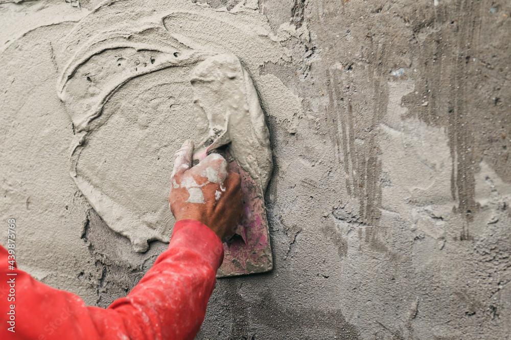 hand of worker plastering cement at wall for building house in construction site.