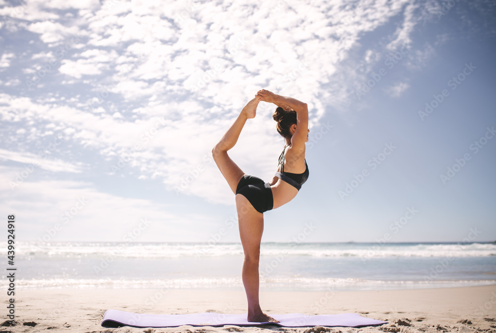 Woman doing Natarajasana yoga pose on the beach