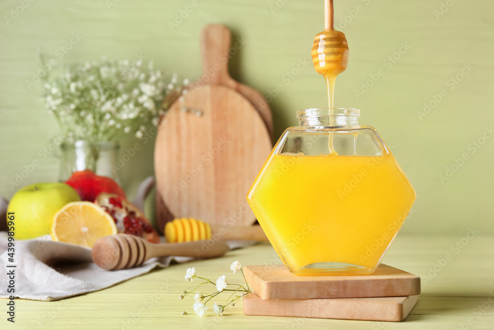 Honey pouring from dipper into glass jar on color background