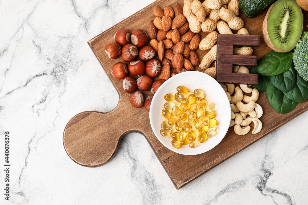 Board with fish oil capsules and healthy products rich in vitamin E on light background