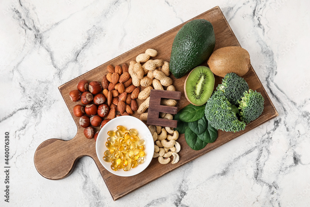 Board with fish oil capsules and healthy products rich in vitamin E on light background