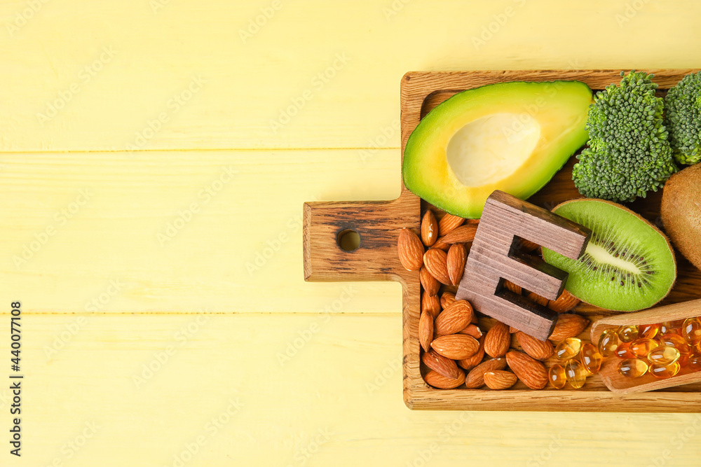 Board with healthy products rich in vitamin E on color wooden background