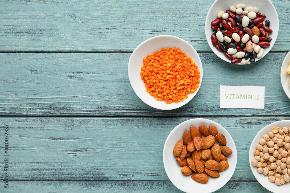 Plates with different healthy nuts and beans rich in vitamin E on color wooden background