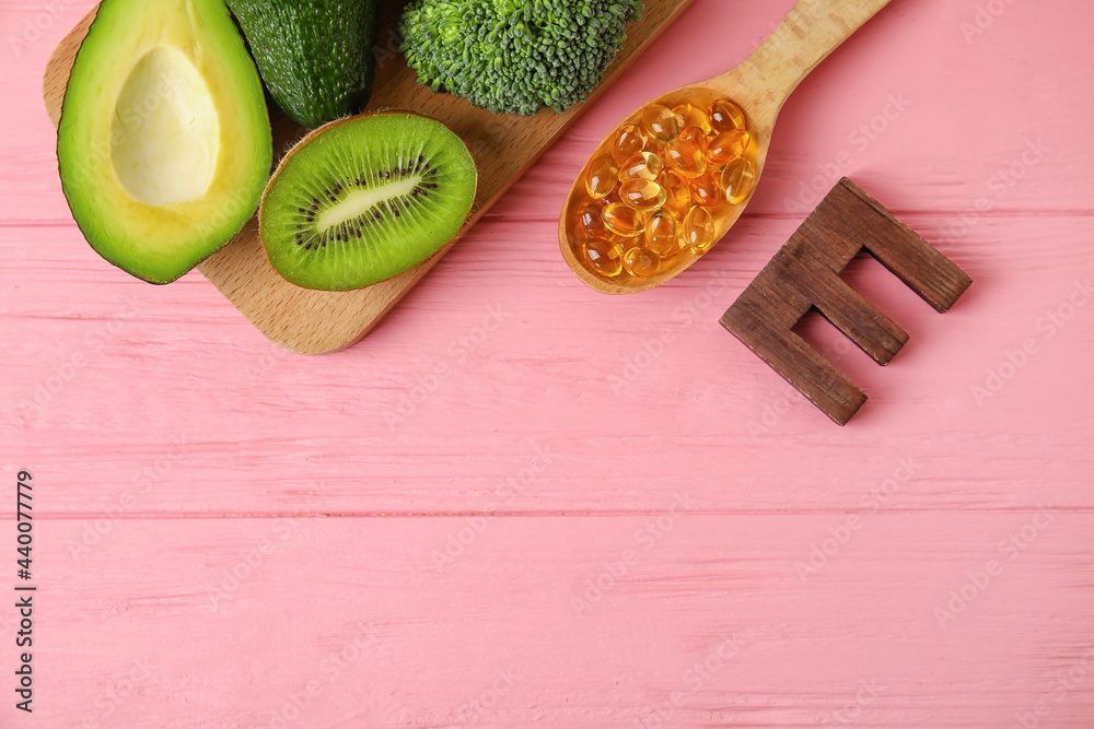 Board with healthy products rich in vitamin E and fish oil capsules on color wooden background