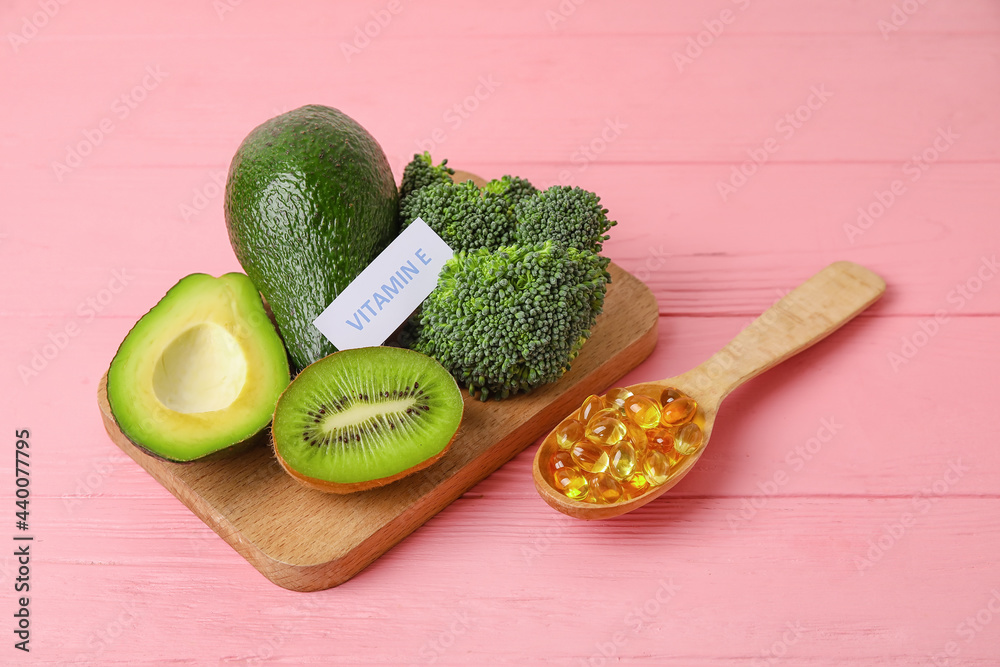 Board with healthy products rich in vitamin E and fish oil capsules on color wooden background