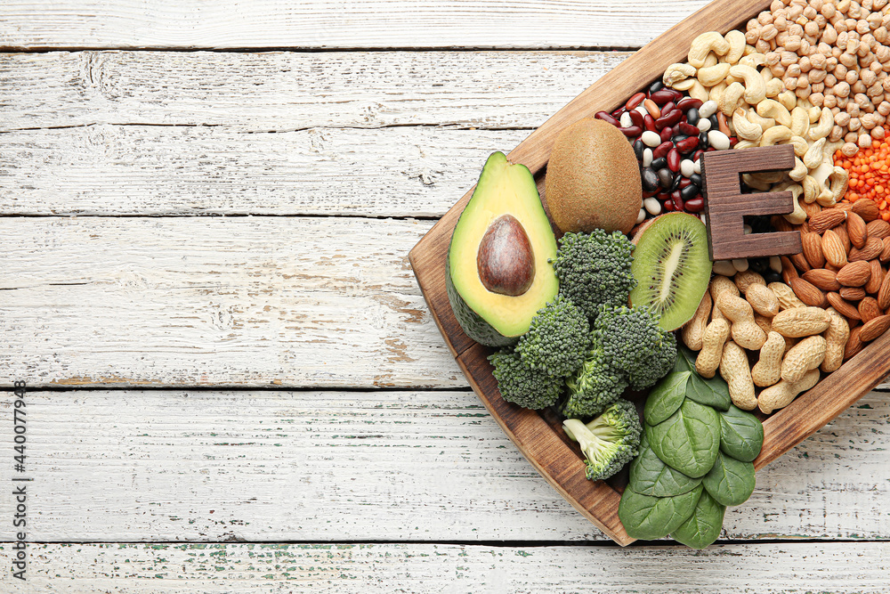 Board with healthy products rich in vitamin E on light wooden background