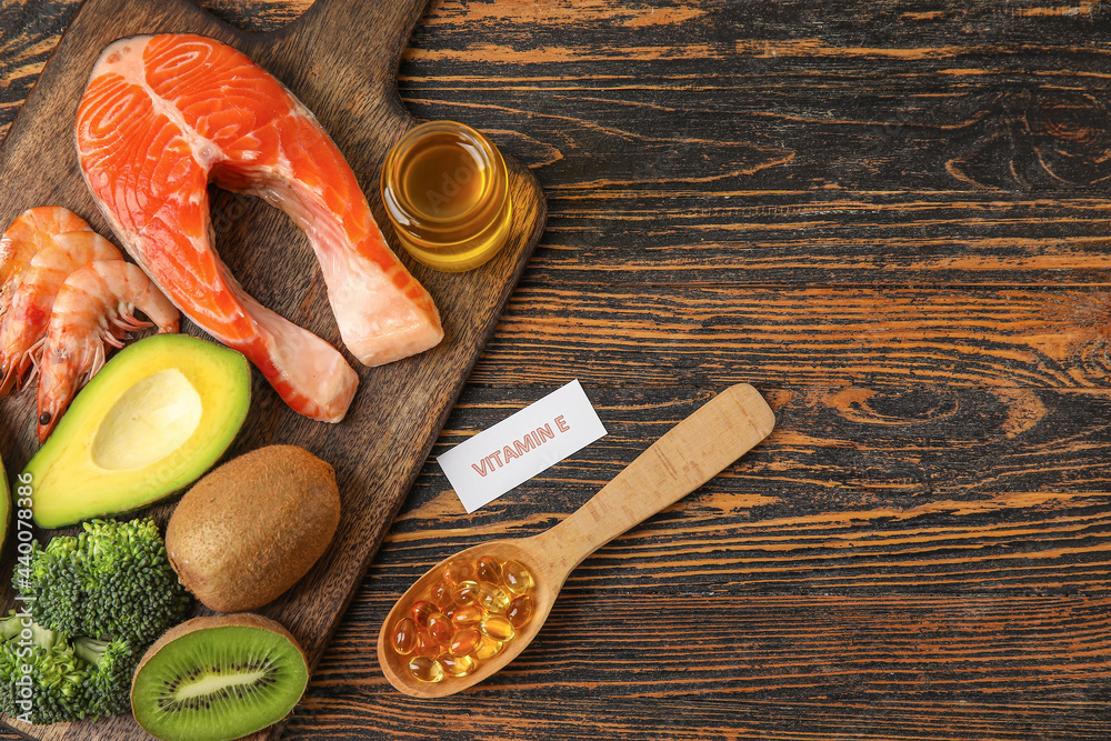 Board with healthy products rich in vitamin E and fish oil capsules on wooden background