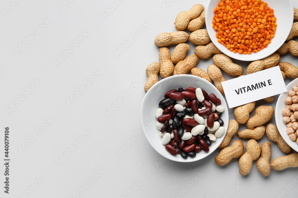 Plates with and different healthy nuts and beans rich in vitamin E on light background