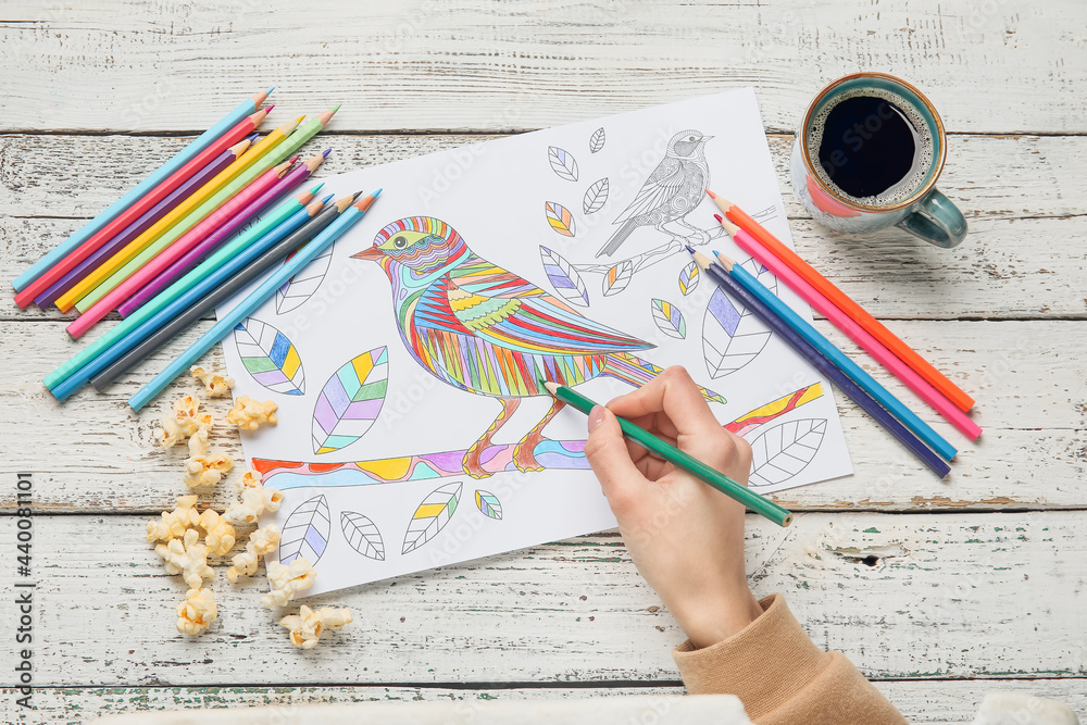 Woman coloring picture at wooden table, closeup