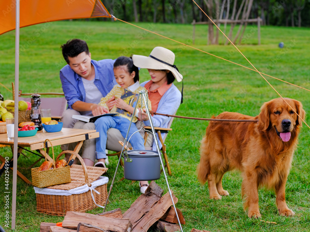 Happy family of three and pet dog reading outside