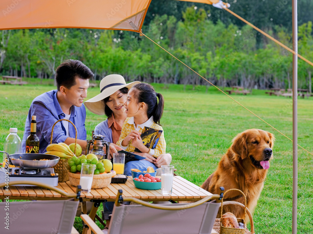 Happy family of three and pet dog reading outside