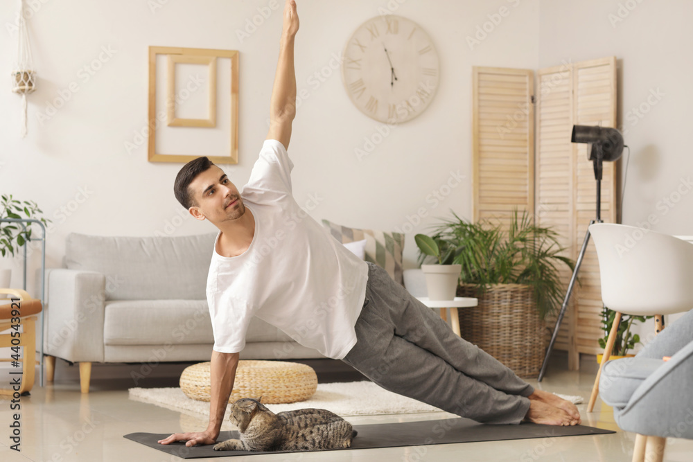 Young man with cute cat practicing yoga at home