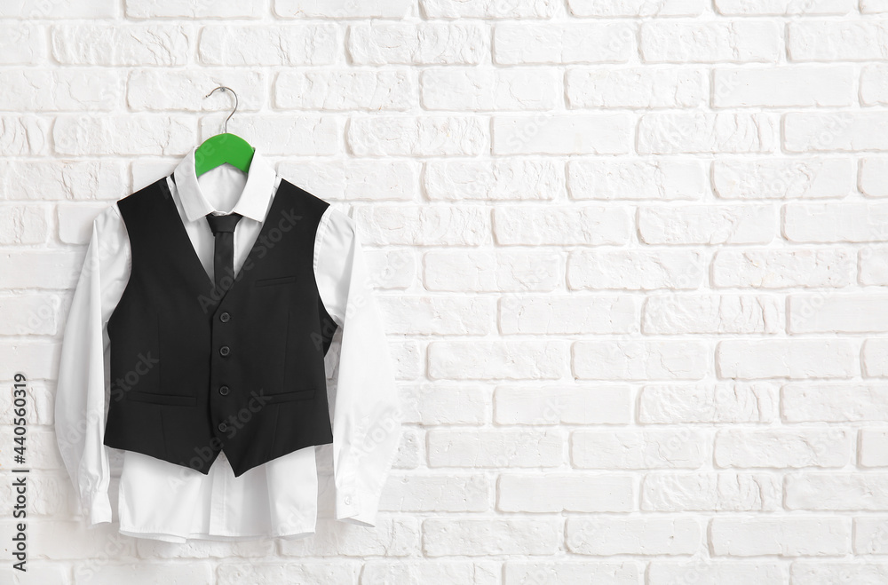 Hanger with stylish school uniform on white brick wall in room