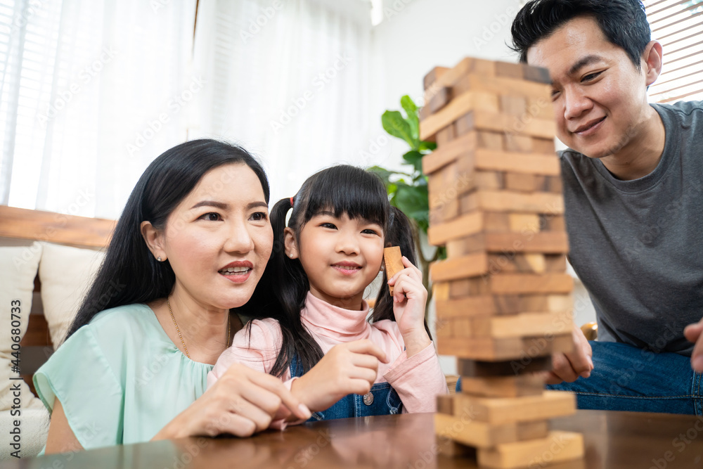 一对亚洲夫妇在家里的客厅里给小女孩玩玩具积木。