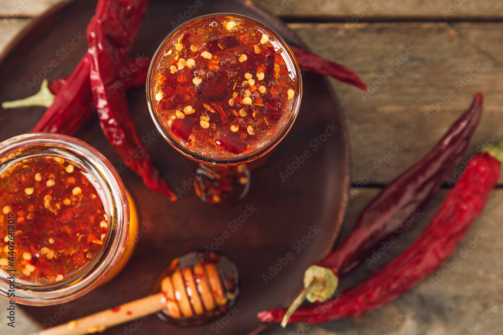 Composition with hot honey and dry chili peppers on wooden background, closeup