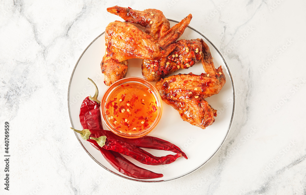 Plate with tasty fried chicken wings, dry chili peppers and hot honey on light background