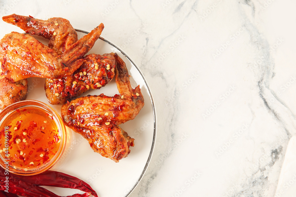 Plate with tasty fried chicken wings, dry chili peppers and hot honey on light background