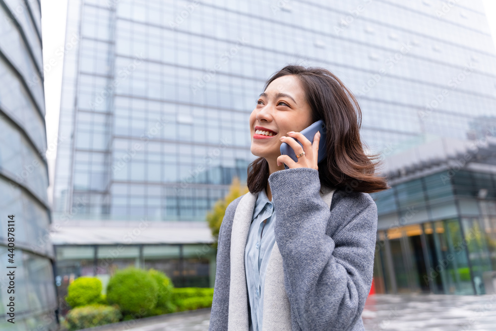 年轻漂亮的女孩在办公楼外用手机开心地给客户打电话