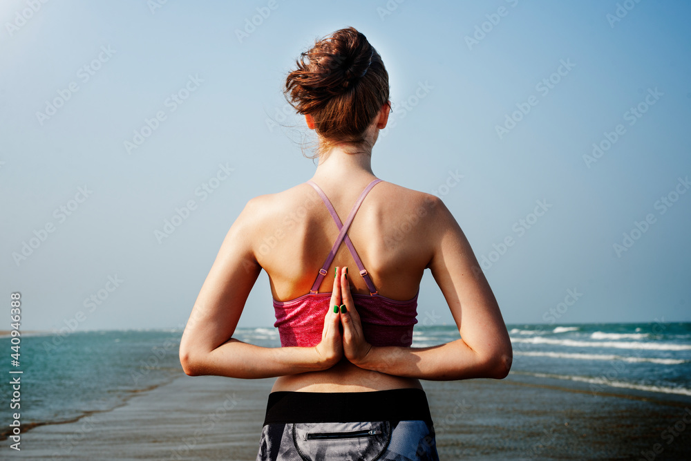 女子在海滩上做反向namaste瑜伽姿势