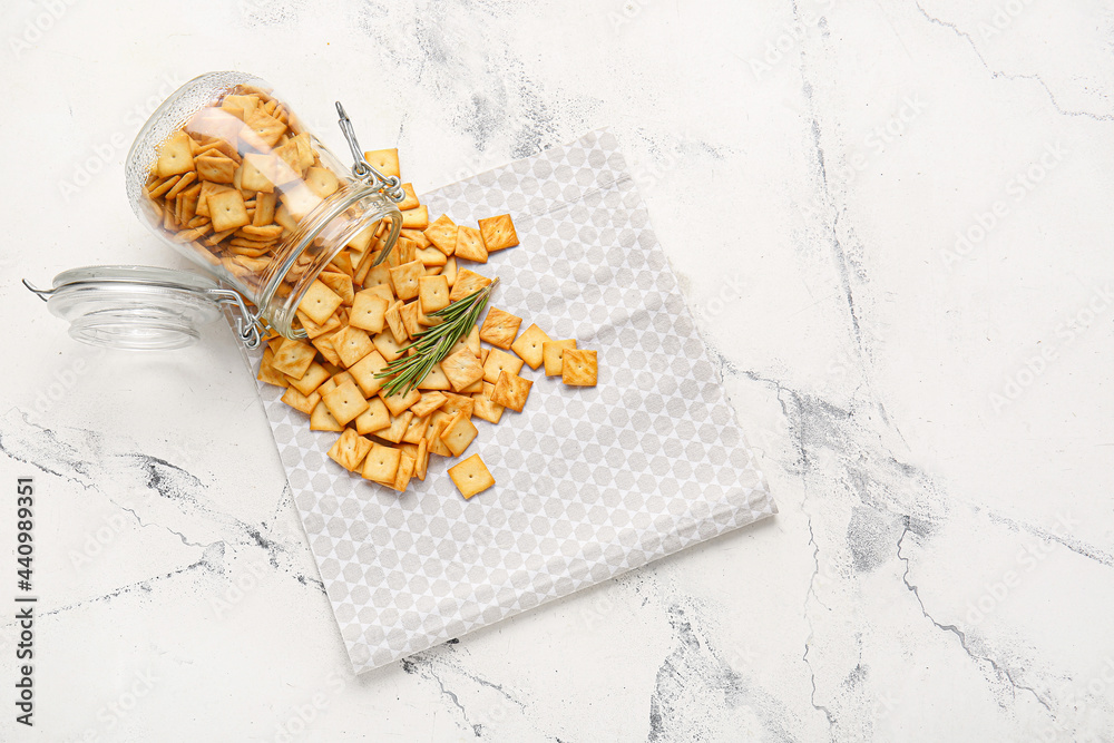 Overturned jar with tasty crackers on light background