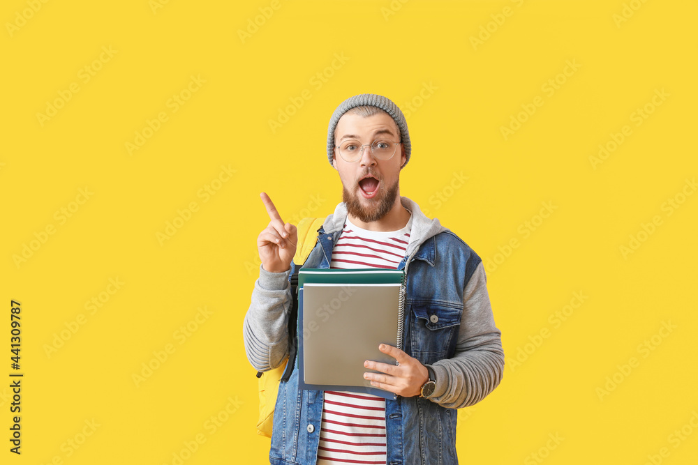 Surprised male student pointing at something on color background