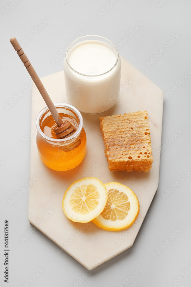 Glass jar with sweet honey, lemon slices, comb and milk on grey background